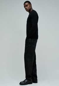 Suéter negro de manga larga combinado con unos vaqueros negros holgados y zapatos negros. El conjunto presenta un diseño simple y una textura suave.