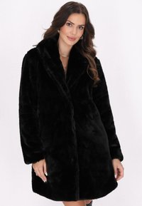 Cappotto in pelliccia sintetica nera con ampio colletto, maniche lunghe e una consistenza morbida. Presenta una vestibilità rilassata e nessuna chiusura visibile.