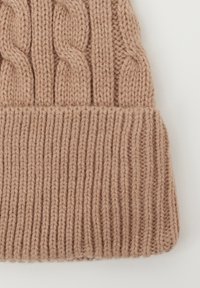 Beige gebreide wollen muts met kabelsteekpatroon en geribbelde, omgevouwen rand, afgebeeld tegen een witte achtergrond.