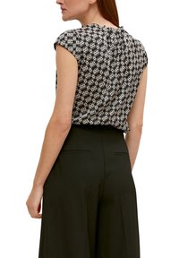 Femme portant un chemisier à manches courtes à motifs noirs et blancs rentré dans un pantalon large noir taille haute, vue de dos.