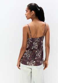 Purple fabric top featuring a floral pattern, thin adjustable straps, and a smocked back for added comfort. Paired with light denim.