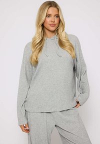 Sudadera gris claro de tela suave y texturizada con capucha ajustable. Corte holgado, mangas largas, combinada con pantalones a juego. Diseño simple.
