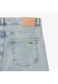 Jeans in denim blu chiaro presentano un'etichetta in pelle in vita e un piccolo logo di coccodrillo verde ricamato sulla tasca posteriore.