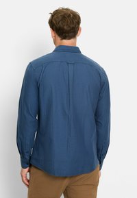 Herren Langarmhemd aus einfarbigem dunkelblauen Stoff mit Button-Down-Kragen und Rückenfalte, ausgestattet mit Knopfmanschetten und einem abgerundeten Saum.