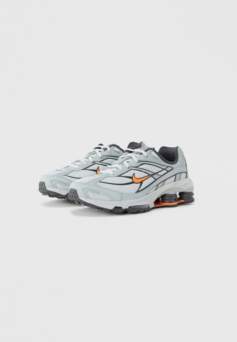 Light grey sneakers with black accents, black mesh lining, and orange logo. Crafted from breathable materials with rounded sole design.