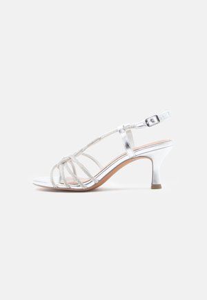 Ασημί σανδάλια με τακούνι, διαθέτουν πλεχτά λουράκια, λαμπερό μεταλλικό φινίρισμα και λεπτό τετράγωνο τακούνι, με λεπτή λουρίδα στον αστράγαλο και αγκράφα.