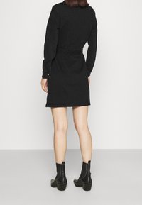 Vestido de mezclilla negra con mangas largas, cinturilla y detalle de botones en los puños. Combinado con botas negras hasta el tobillo con un tacón grueso.