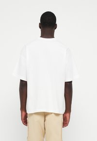 White short-sleeve T-shirt made of cotton with a relaxed fit, featuring a crew neck and a smooth texture, viewed from the back.