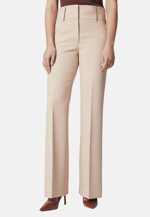 Beżowe spodnie w kant z wysokim stanem, szerokimi nogawkami i detalami w postaci zakładek, zestawione z brązowymi czółenkami na szpilce.