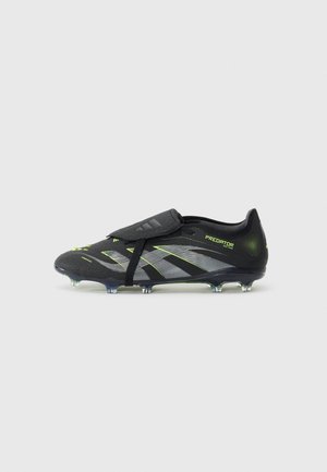 Bota de fútbol Adidas Predator negra con detalles en plata y verde neón, con tacos y sistema de cordones cubierto sobre un fondo blanco.