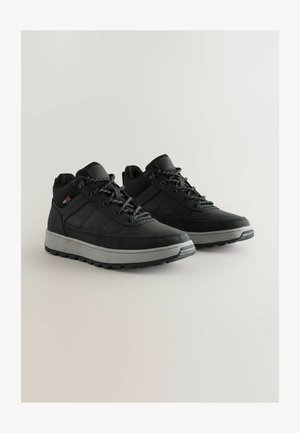 Fekete túracipő pár szürke talppal és fényvisszaverő fűző részletekkel világos háttéren.