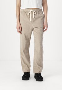 Pantalones de pana beige con costillas verticales, cinturilla elástica y detalle de cordón. Corte holgado y diseño de pierna recta.