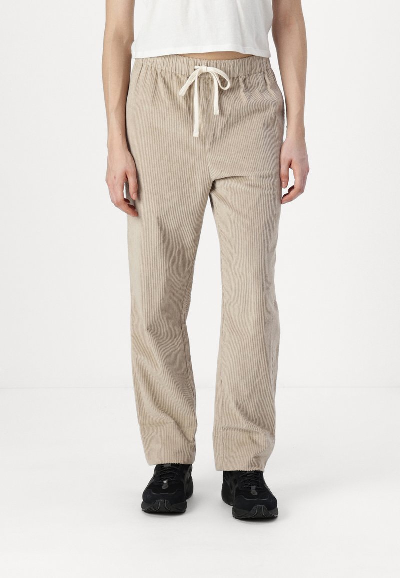 Pantalones de pana beige con costillas verticales, cinturilla elástica y detalle de cordón. Corte holgado y diseño de pierna recta.