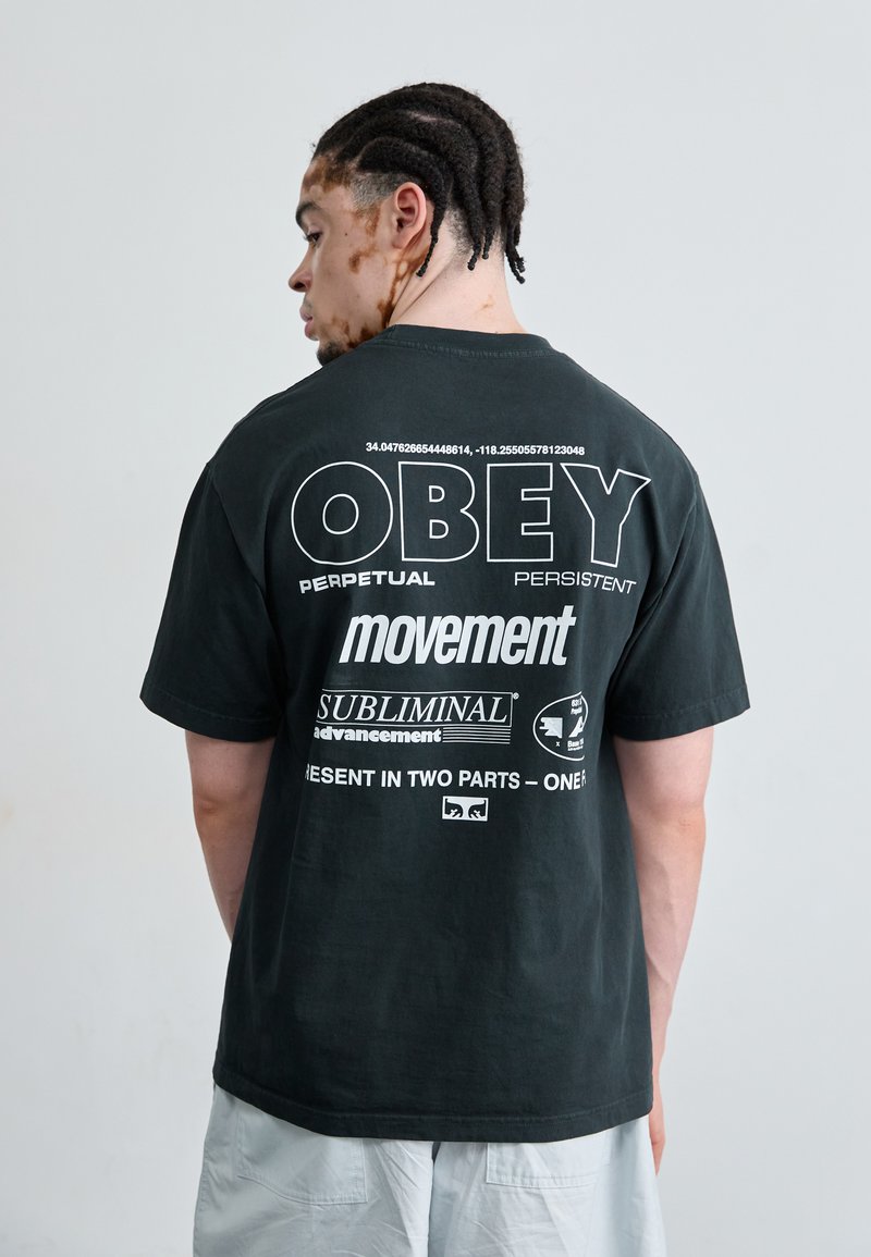 T-shirt en coton noir avec un texte graphique au dos en blanc. Présente une coupe surdimensionnée, un col rond et des manches courtes.