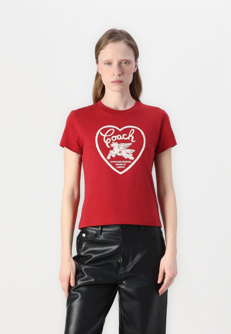 Camiseta de algodón roja con mangas cortas, que presenta un gráfico blanco en forma de corazón con la palabra "Coach" y una ilustración de un caballo alado.