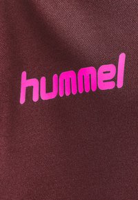 Mörkröd textil med en slät yta som har en framträdande rosa "hummel"-logotyp i en djärv, modern stil.