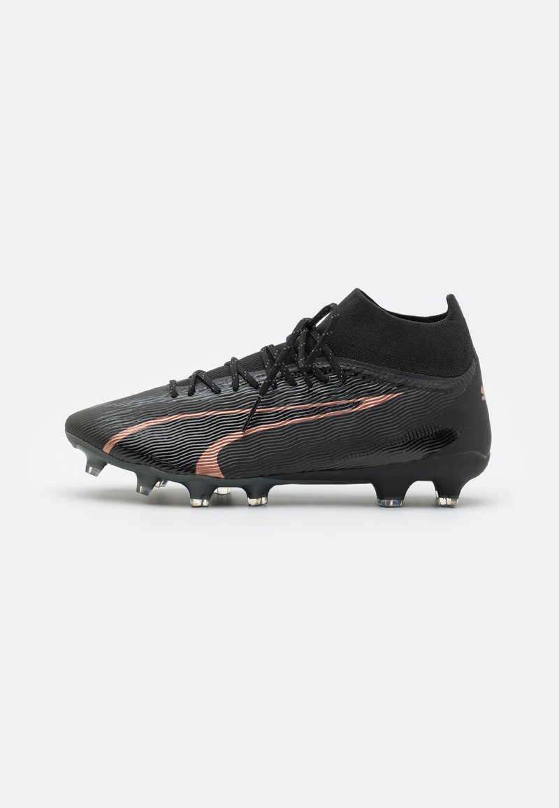 Botas de fútbol negras con una parte superior texturizada, que presenta una franjas de cobre prominente. Diseño elegante, collar tipo calcetín y tachuelas metálicas para tracción.