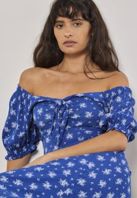 Blå off-shoulder kjole med puffærmer, blomsterprint, samlet front med bånddetalje og en let, svajende silhuet, lavet af let stof.