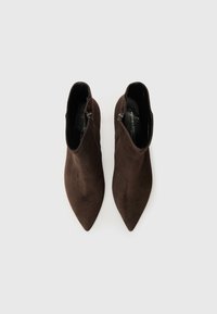Bottes chevilles en daim marron avec des pointes en biais, des fermetures éclair sur les côtés et une texture lisse, présentant un design épuré et minimaliste.