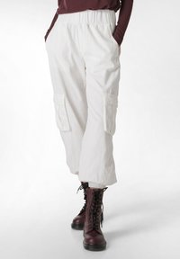 Witte cargo broek met elastische tailleband, grote zijzakken en een ontspannen pasvorm, gecombineerd met burgundy veterschoenen.
