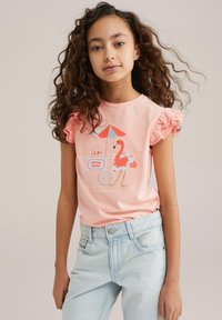 Camisa rosa de manga corta con volantes en las mangas, que presenta un diseño bordado de un flamenco y un carrito de helados. Jeans de mezclilla claros con un ligero desgaste.