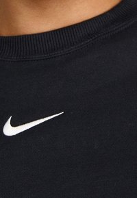 Black cotton sweatshirt with a ribbed neckline and a white Nike swoosh logo positioned on the front. Smooth texture and casual design.