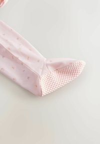 Ljusrosa bomullsstrumpa med små blommönster. Sulan har texturerade greppunkter för bättre fäste. Mjukt tyg med en enkel design.