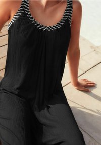 Vestido negro con una tela texturizada, que presenta un escote con cuentas y tirantes anchos. El vestido fluye suavemente, resaltando una silueta relajada.