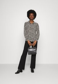 Blusa preta de flores com fecho à frente, mangas longas; combinada com calças pretas decadentes e uma pequena mala preta; botas brilhantes completam o visual.