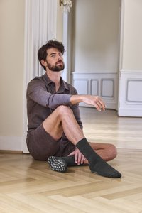 Šedé tričko s dlouhým rukávem a odpovídající šortky, sedící na dřevěné podlaze; na nohou tmavé ponožky s texturovanou gumovou podrážkou a puntíkovaným vzorem.