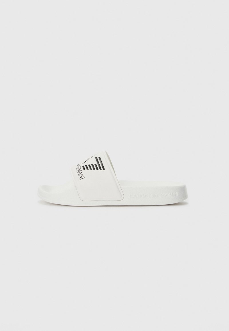 Bela drsna sandal z značilnim pasom in črnim logotipom, gladkim podplatom in gumijastim podplatom. Minimalističen oblikovalski slog s čistimi linijami.
