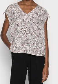 Haut ample à manches courtes en tissu léger. Présente un décolleté en V et un motif abstrait multicolore en rose, noir et blanc.