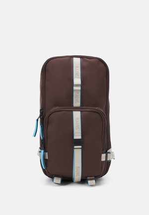 Bruine rugzak met twee voorzakken met rits, blauwe en beige schouderbanden, en een gladde buitenstof. Stevige onderkant voor stabiliteit.