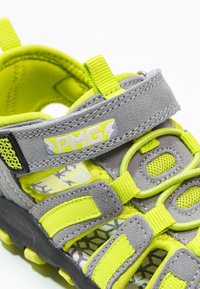 Grey and neon yellow athletic sandal featuring suede material, adjustable straps, mesh vents, and patterned insoles for breathability.
