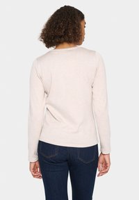 Haut beige clair à manches longues avec un col rond et des poignets côtelés, associé à un jean bleu foncé. Le tissu semble doux et texturé.