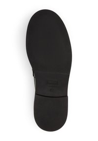 Semelle de chaussure noire plate avec une surface texturée. Présente un détail de logo rectangulaire et des bords lisses. Principalement en matériau en caoutchouc.
