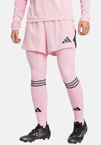Completo sportivo rosa con maglietta a maniche lunghe e pantaloni corti, con accenti neri, righe verticali sulle calze e scarpe sportive nere.