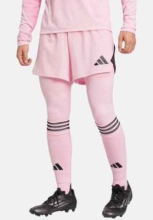 Rosa Sportkleidung mit einem Langarmoberteil und Shorts, ausgestattet mit schwarzen Akzenten, vertikalen Streifen auf den Socken und sportlichen schwarzen Schuhen.