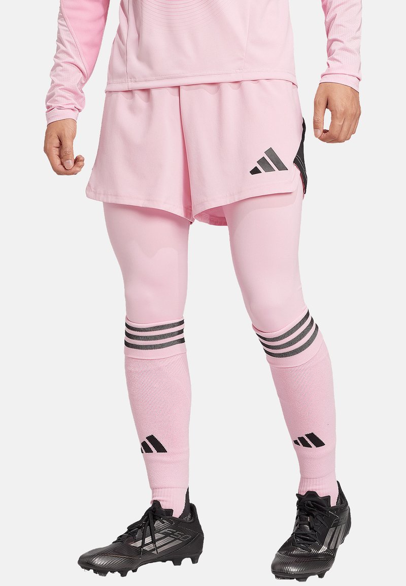 Roze sportoutfit met een langarmtop en shorts, met zwarte accenten, verticale strepen op de sokken en sportieve zwarte schoenen.