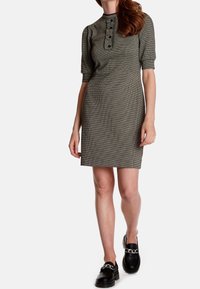 Klänning med hundtandsmönster i grått och svart, med korta ärmar, rund halsringning och knapppdetaljer fram. Bärs med svarta loafers.