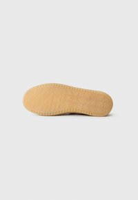 Semelle de chaussure en caoutchouc avec une surface texturée, présentant des motifs en zigzag et des logos en relief. Couleur brun clair avec un design durable offrant une bonne adhérence.