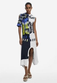 Asümmeetriline kleit mitmevärviliste graafiliste trükkidega, lühikeste varrukatega, kõrge lõhikuga, valmistatud siledast kangast, sinise, musta, valge ja kollase toonidega.