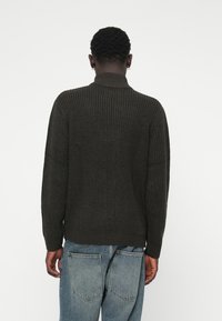 Dark gray knitted sweater with a high collar and ribbed texture, featuring dropped shoulders and long sleeves. Paired with light denim jeans.