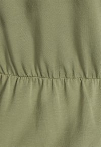 Tecido verde com uma textura suave, apresentando costura franzida ao longo da cintura. Design simplista sem padrões ou acessórios adicionais.