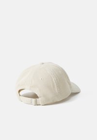 Beige corduroy cap with a curved brim, adjustable strap at the back, and textured ridges on the fabric. No notable patterns or designs.