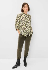 Shirt met een groen en bruin zebra patroon, hoge kraag en opgeblazen mouwen; gecombineerd met olijfgroene corduroy broek en zwarte enkellaarsjes.