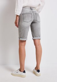 Shorts en denim gris avec ourlets retroussés, comportant deux poches arrière. Portés avec des baskets blanches aux accents bleu marine. Texture lisse, design décontracté.