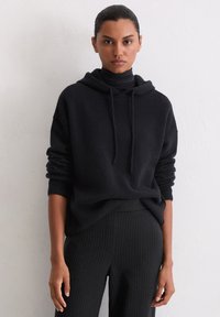 Czarna bluza z kapturem z miękkiego materiału, o luźnym kroju, z prążkowanymi mankietami i warstwowym wyglądem z czarnym golfem pod spodem.