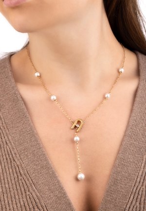 Goldene Kettennacklace mit einem stilisierten Anhänger und abwechselnden weißen Perlen, das ein einfaches, aber elegantes Design präsentiert. Die Kette hat eine zarte Textur.