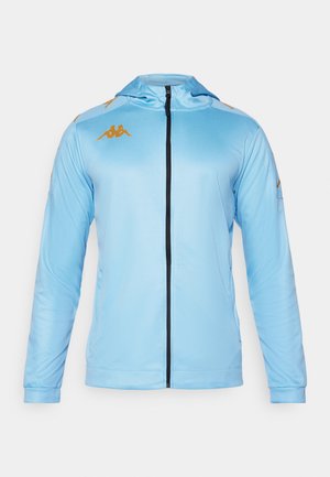 Veste à zip bleu clair avec des manches longues, dotée d'une capuche, d'un zip noir et d'accents de logo dorés sur les épaules. Tissu lisse et athlétique.